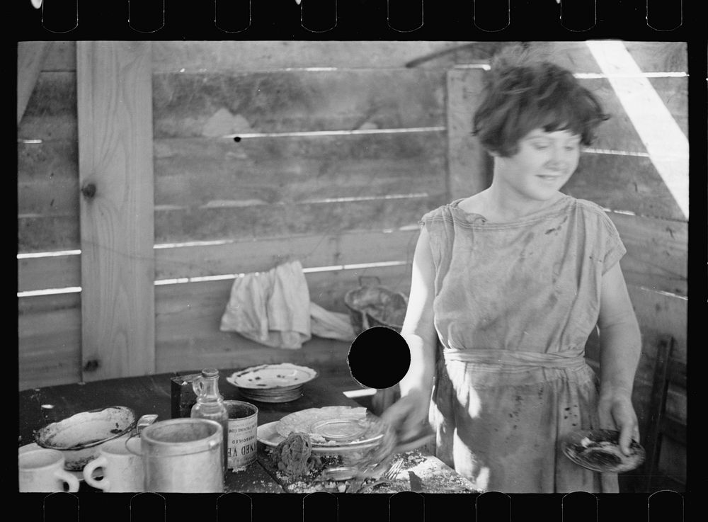 [Untitled photo, possibly related to: Twelve-year old girl of family of nine, cooking meal in rude, open lean-to near hut…