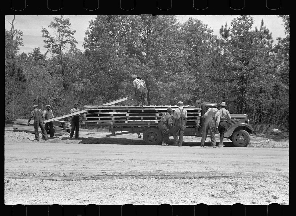 Unloading parts of prefabricated house, preparatory to erecting, Roanoke Farms, North Carolina. Sourced from the Library of…