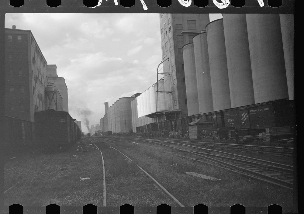 [Untitled photo, possibly related to: Freight cars at grain elevator with lumber used for boarding up carloads of grain…