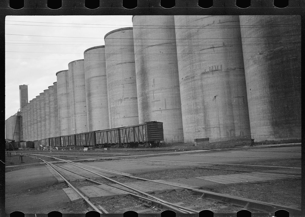 [Untitled photo, possibly related to: Freight cars at grain elevator with lumber used for boarding up carloads of grain…