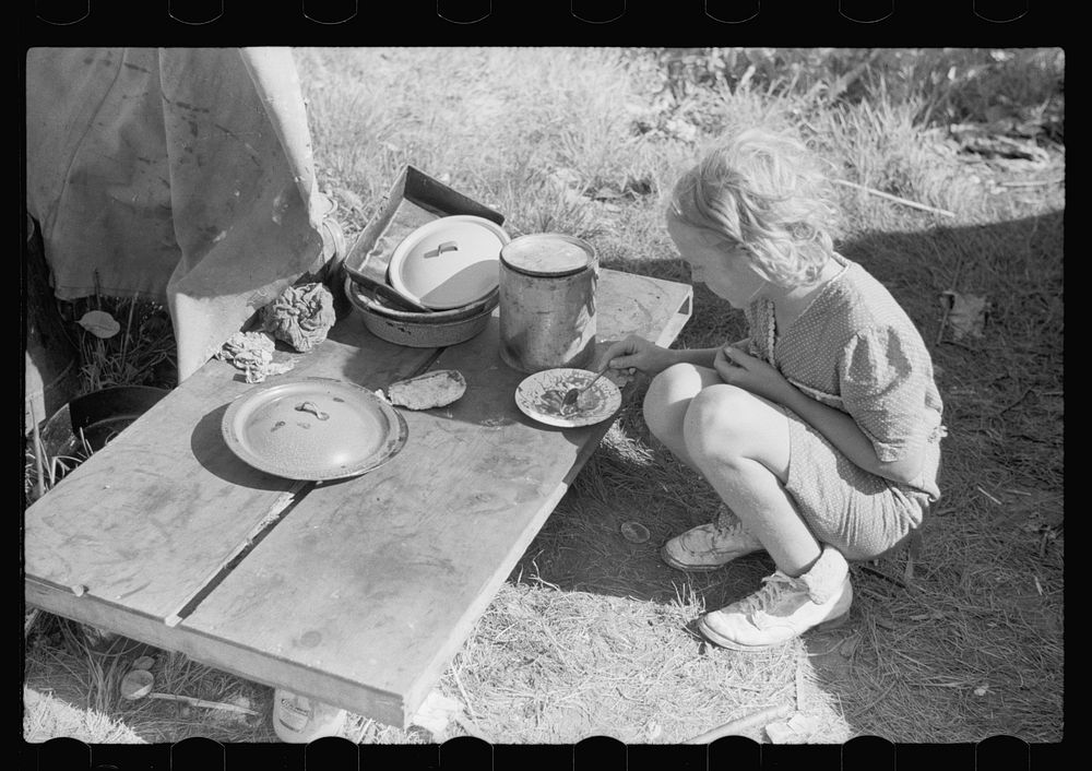 Migrant child eating in front of tent home, Berrien County, Michigan. Sourced from the Library of Congress.