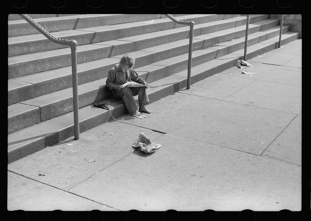 Boy reading funny paper on steps of public library, Milwaukee, Wisconsin. Sourced from the Library of Congress.