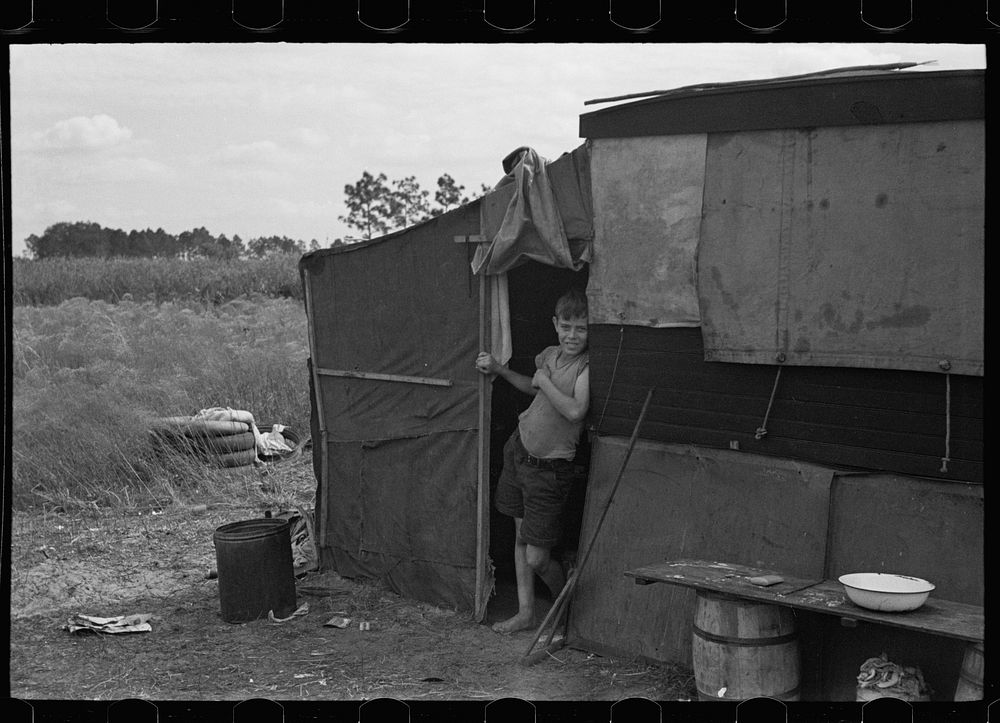 Son of a migrant family in the doorway of his temporary home near Winter Haven, Florida. Sourced from the Library of…