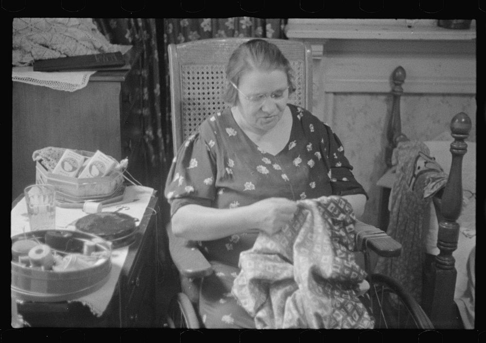 Washington, D.C. A woman doing handwork in her bedroom. Some hand-crochet work is lying on a dresser back of her and also in…