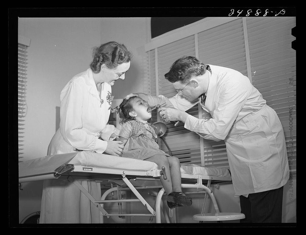 Doctor in clinic with young patient. Robstown FSA (Farm Security Administration) camp, Texas. Sourced from the Library of…