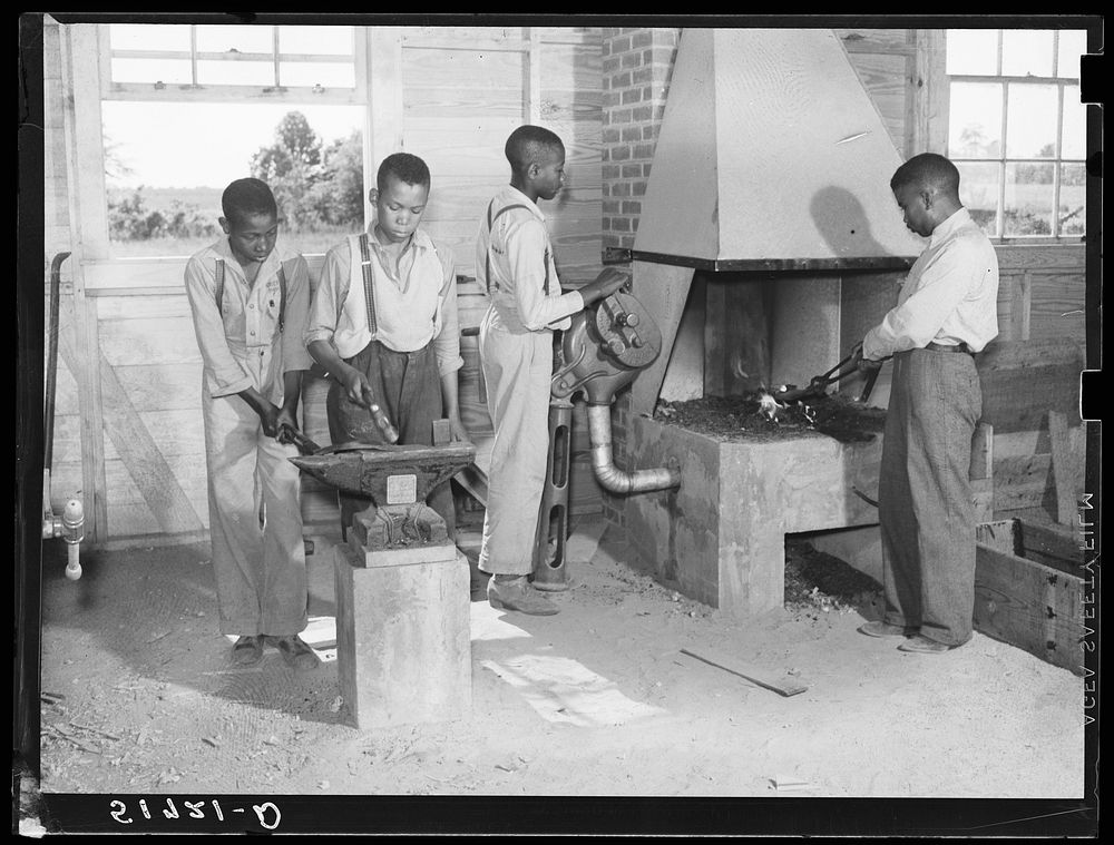 O.C. Cramer, Frederick West, J.W. West and another student sharpening plow point at forge in school shop. Flint River Farms…