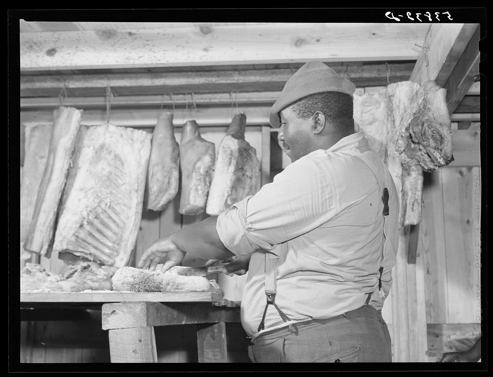 [Untitled photo, possibly related to: Lewis Wiggins cutting off a slice of homecured ham in his smokehouse. La Delta…