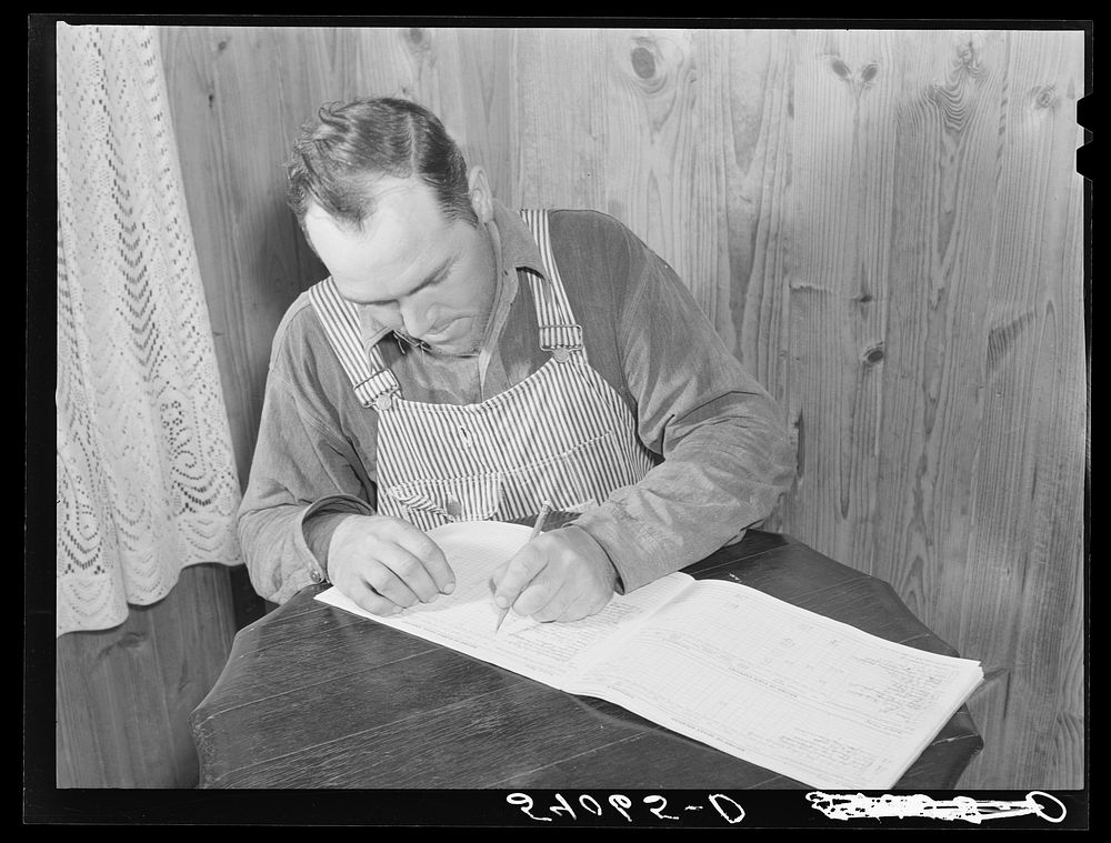 Mr. Verden Lee working on the farm family record book in his home. Transylvania Project, Louisiana. Sourced from the Library…