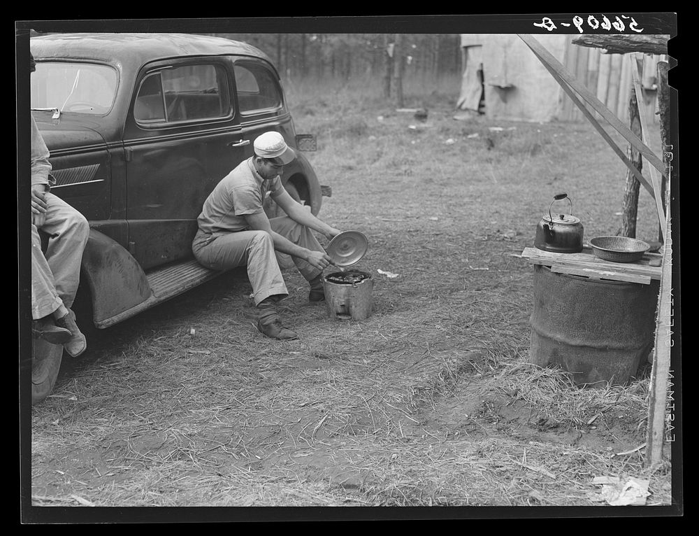 [Untitled photo, possibly related to: John H. Poole, Jr. cooking while sitting on side of car. He is a carpenter on…