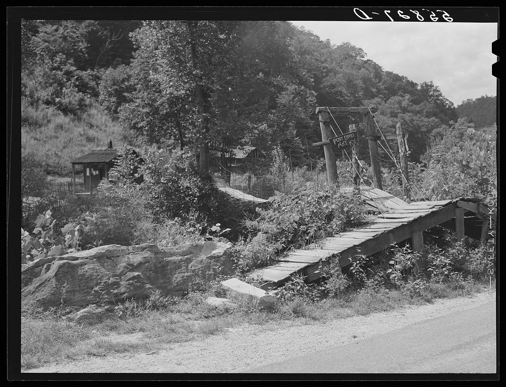 Swinging bridge crossing over creek from main road to post office and store. Ary, Kentucky. Sourced from the Library of…