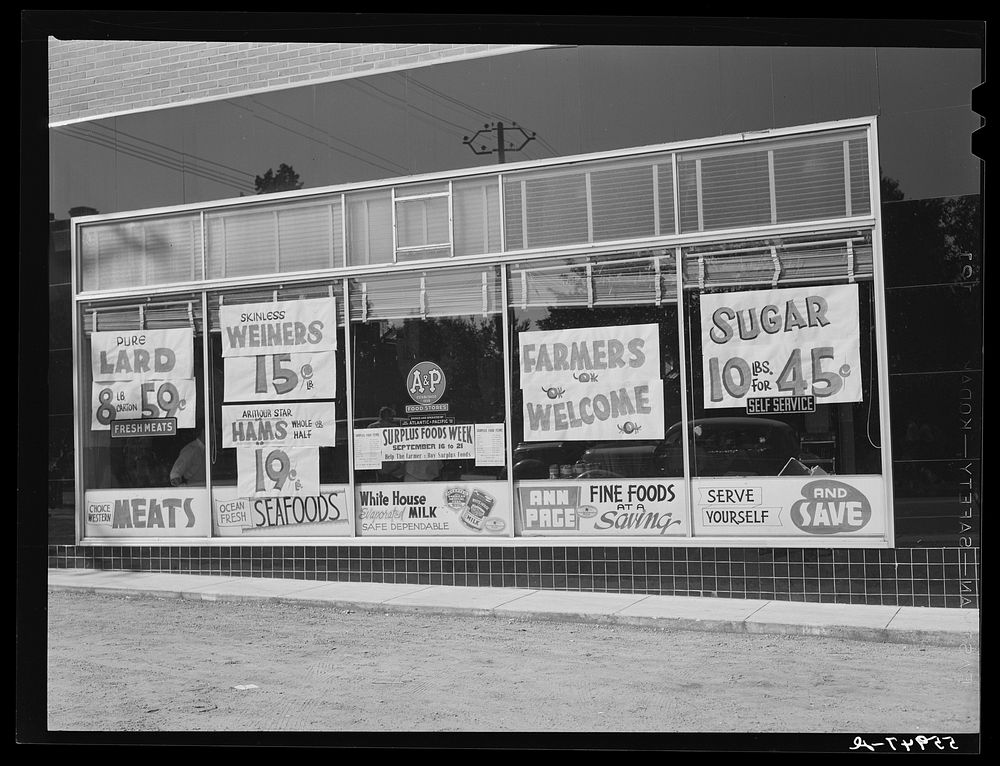 Signs on chain store window welcoming farmers to town during tobacco auction sale time. Sourced from the Library of Congress.