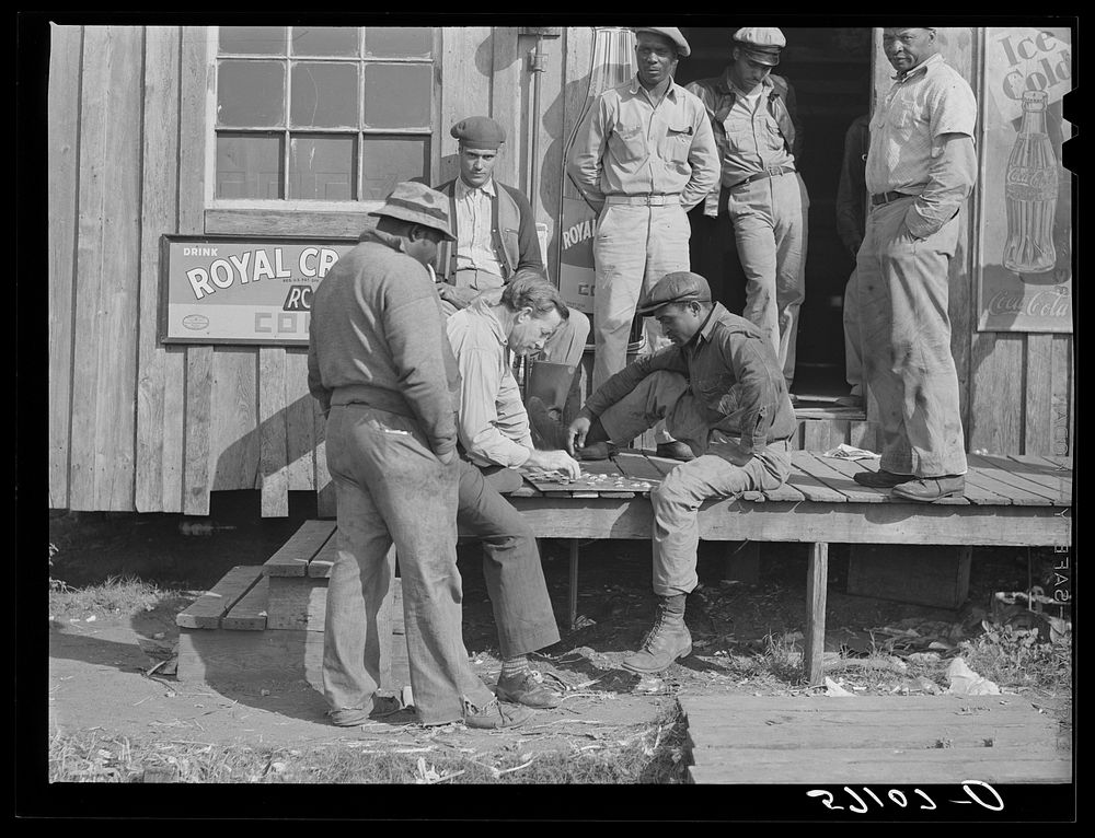 [Untitled photo, possibly related to: Migratory laborers playing checkers in front of juke joint during slack season for…