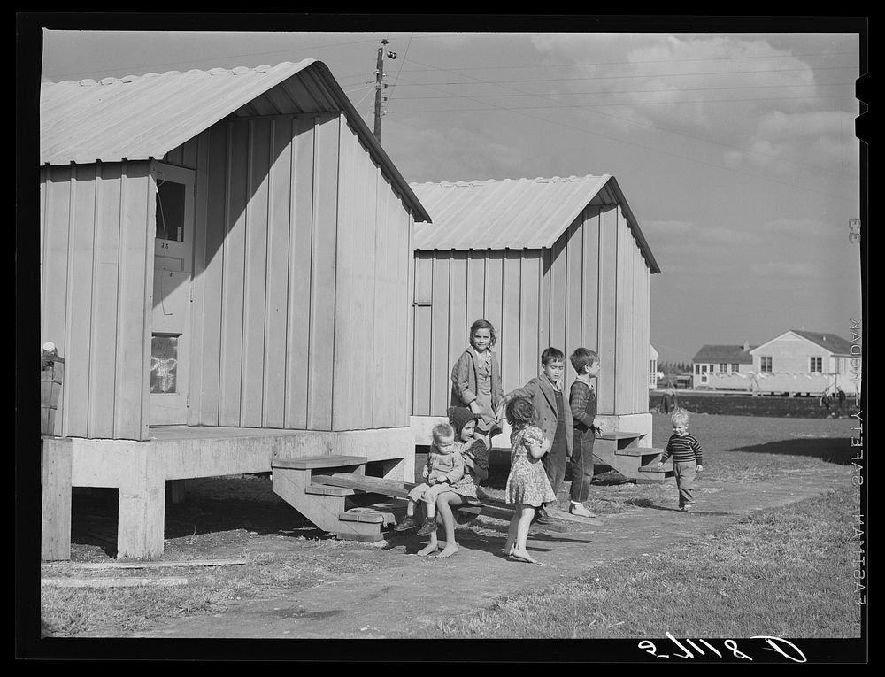 Children of migrant packing house workers in front of metal shelters at Osceola migratory labor camps built by FSA (Farm…