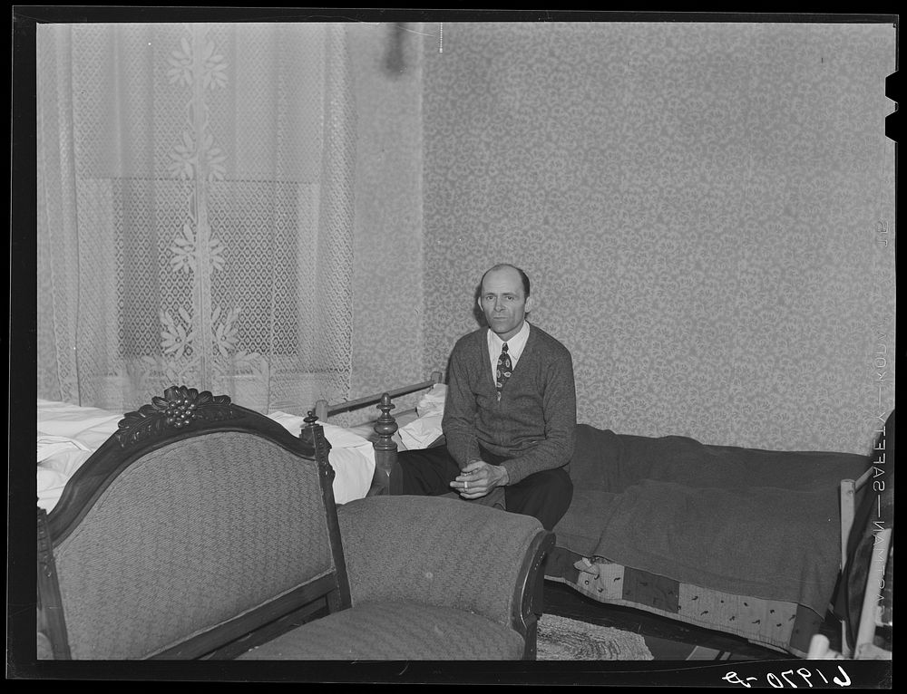 Carpenter on his bed in room which he shares with another Hercules worker. Radford, Virginia. Sourced from the Library of…