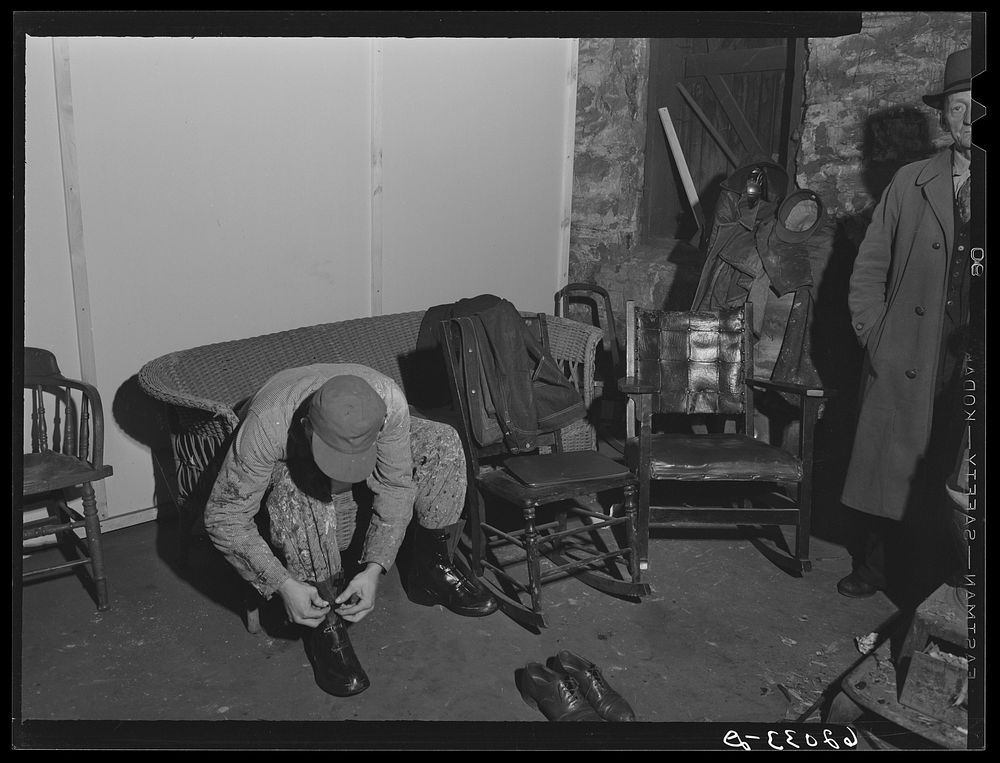 Constuction worker putting on overshoes in basement of Mr. Tilly's secondhand furniture store where he rents a room.…
