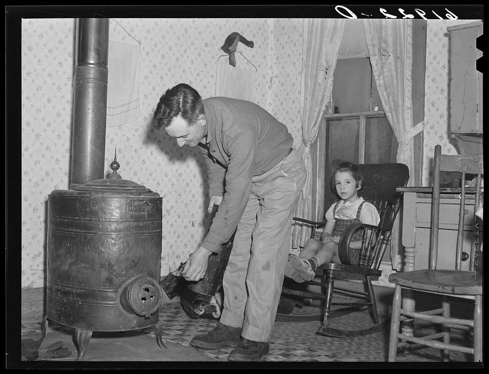 Rehabilitation borrower putting log in stove. Labette County, Kansas. Sourced from the Library of Congress.