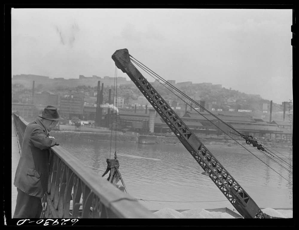 Man watching steamshovel unload sand from barges. Pittsburgh, Pennsylvania. Sourced from the Library of Congress.