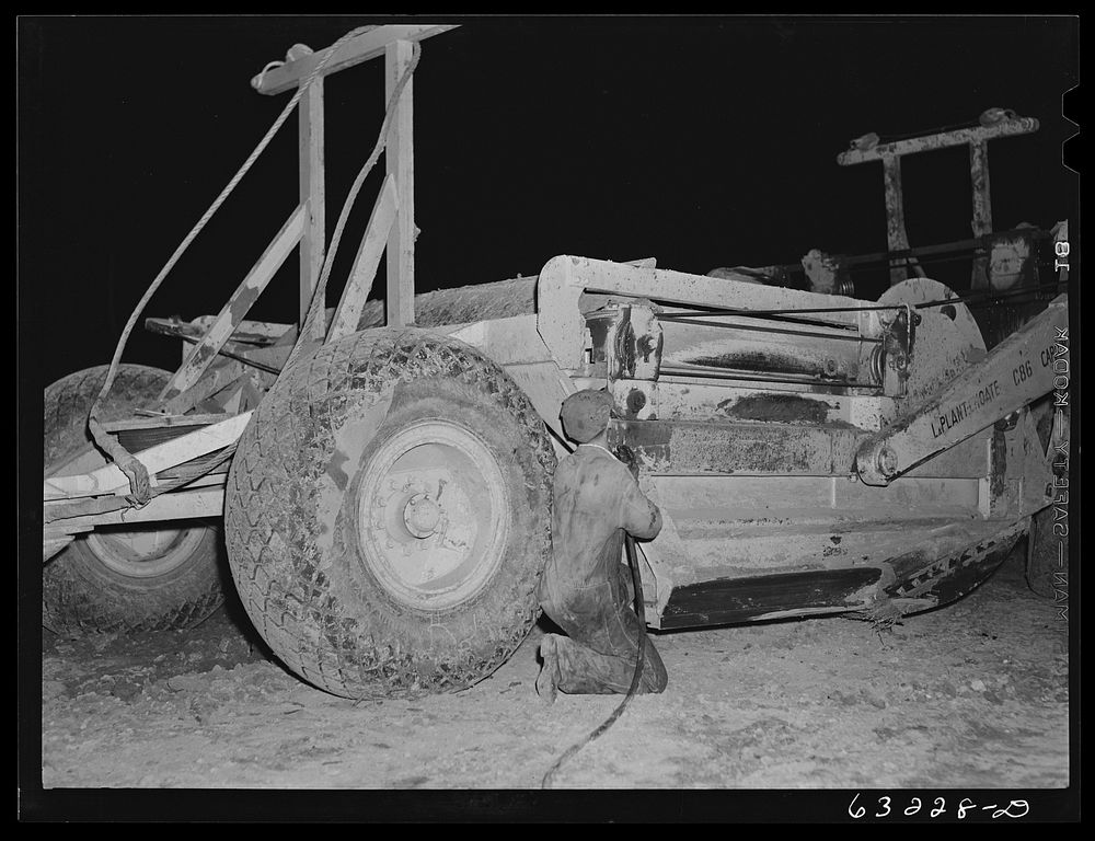 Member of road construction gang greasing "cats" at night. Grant County, Wisconsin. Sourced from the Library of Congress.