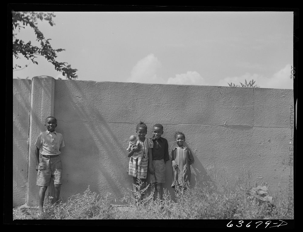  children standing in front of half mile concrete wall, Detroit, Michigan. This wall was built in August 1941, to separate…