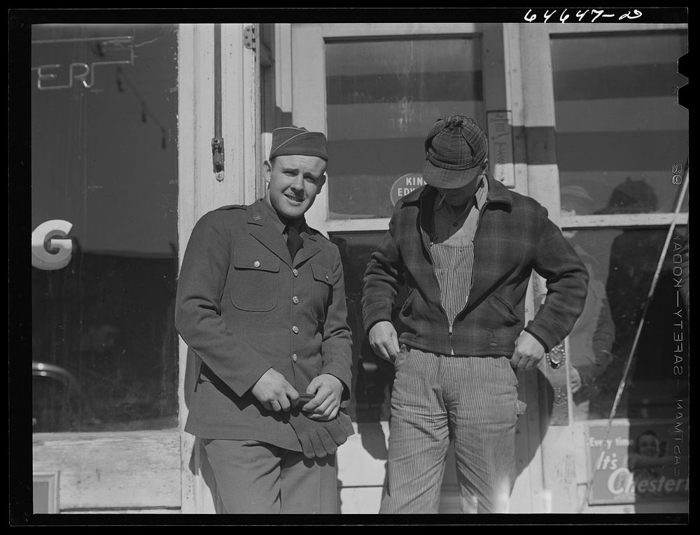 Bowdle, South Dakota. Soldier home on furlough, talking with friend in front of pool hall. Sourced from the Library of…