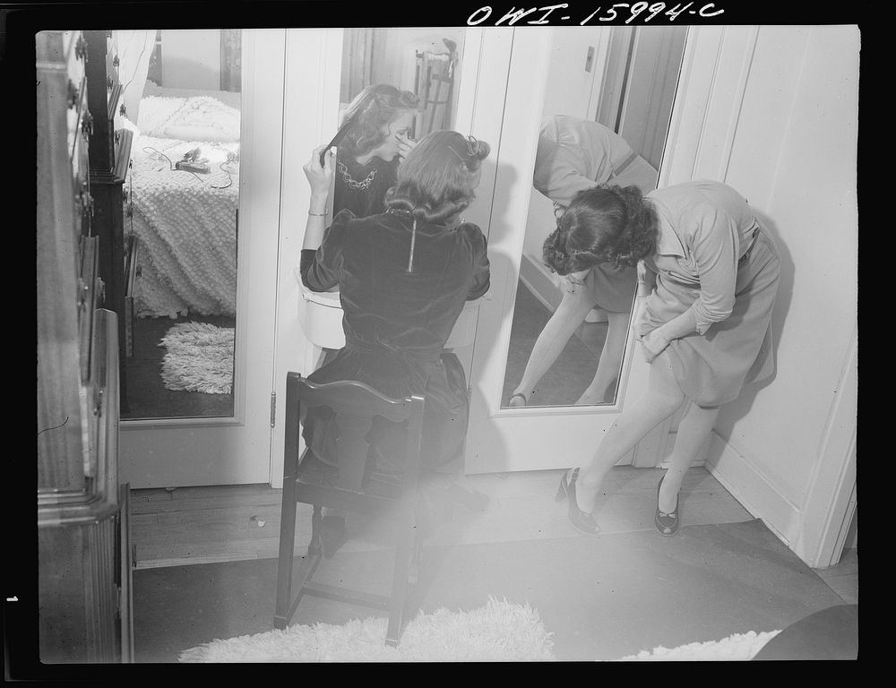 [Untitled photo, possibly related to: Detroit, Michigan. Girl putting on lipstick and another girl straightening seams in…