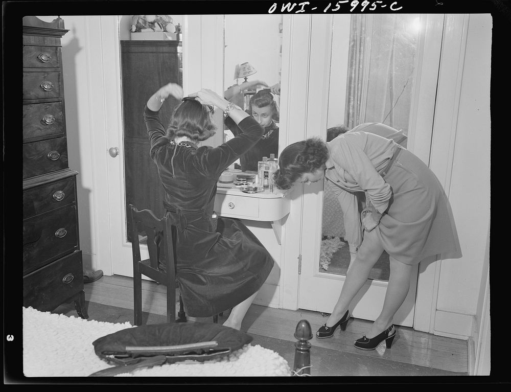 Detroit, Michigan. Girl straightening seams in her stockings and another girl combing her hair in a mirror. Sourced from the…
