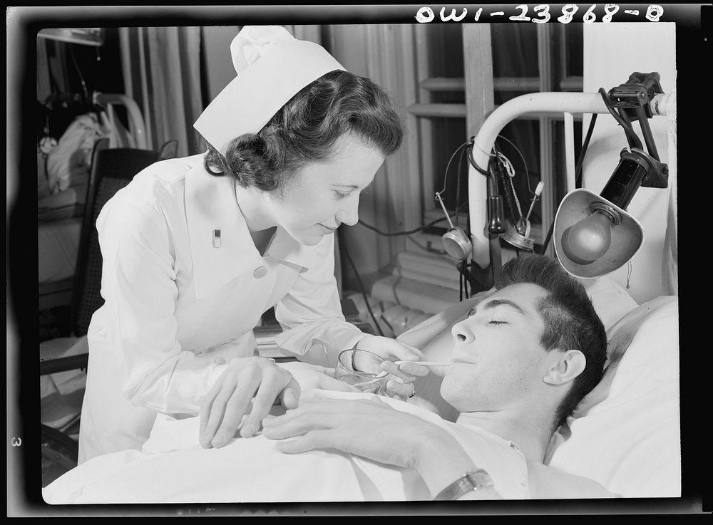 Encased in a body and leg cast, this soldier must have constant care. Here, Army nurse Frances Bullock helps him to a drink…