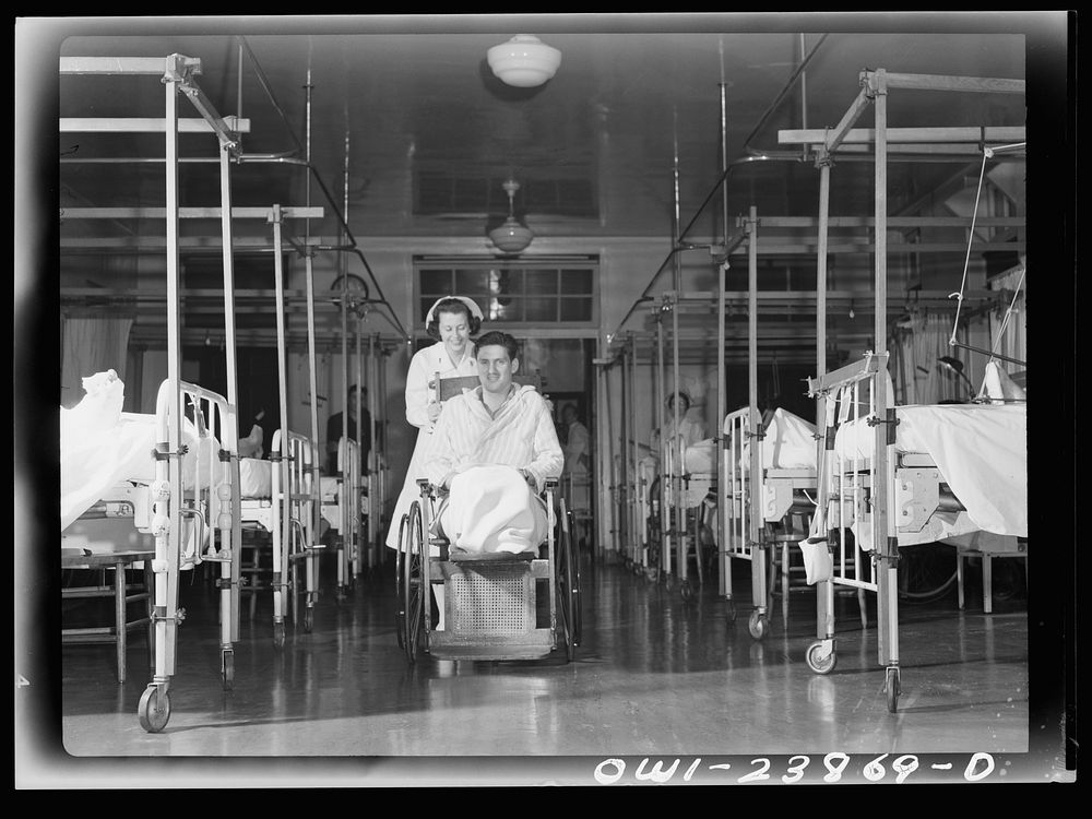 Nurse Frances Bullock wheels a wounded soldier back to his bed in the orthropedics ward of an Army hospital. Sourced from…