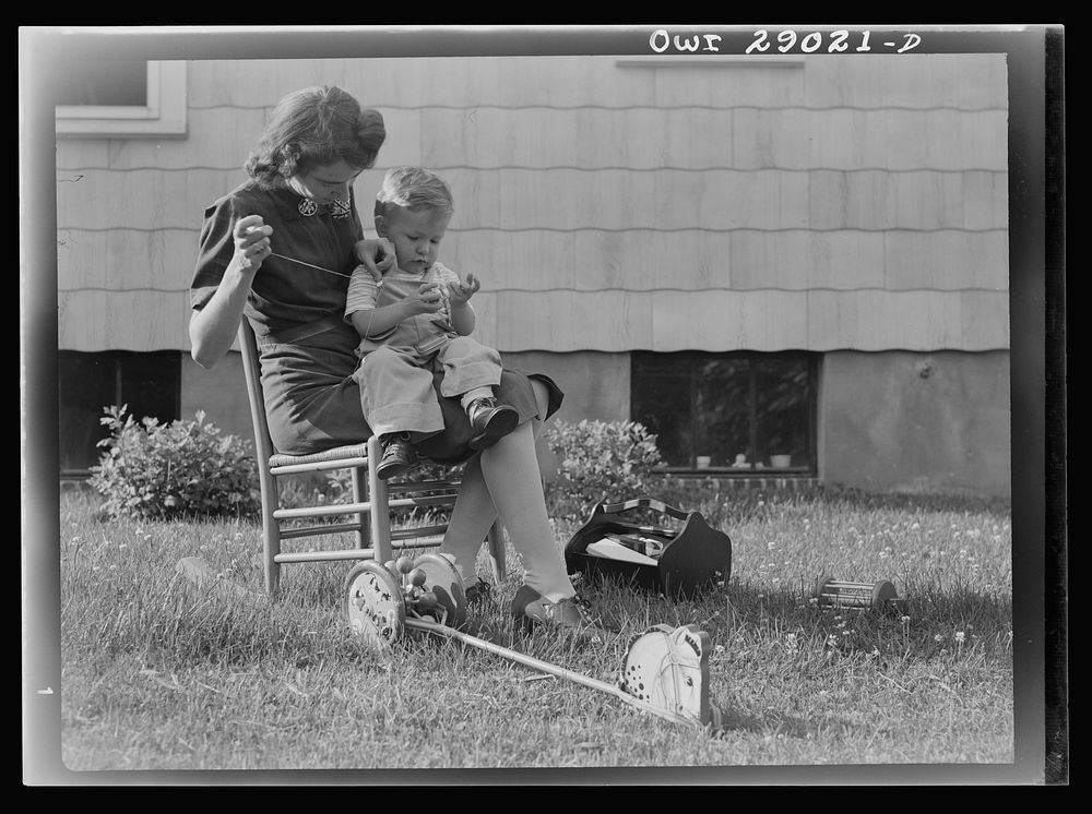 A mother sewing a button on her child's overalls. Silver Spring, Maryland. Sourced from the Library of Congress.