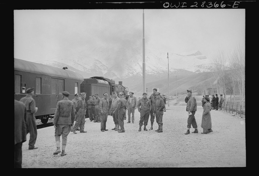 American and British soldier trainmen standing about at a station on the route for supplies to Russia. An American engine is…