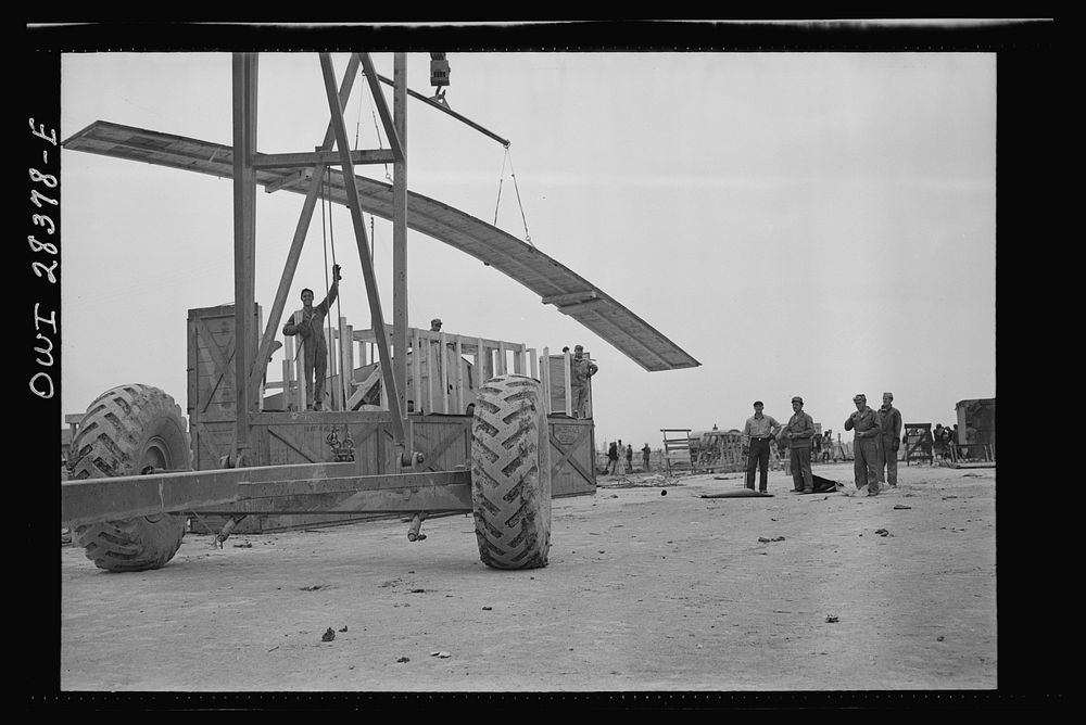 Mobile crane lifting the top from a crate containing a United States fighter plane awaiting assembly at the assembly…