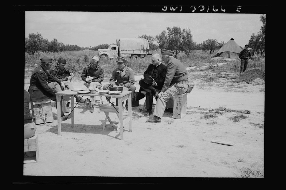 Archbishop Spellman of New York dining at a fighter base of the U.S. Army 9th Air Force somewhere in Tunisia. Left to right:…
