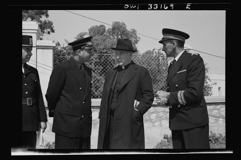 Sfax, Tunisia. Archbishop Spellman of New York talking with French officials on the streets. The official with the braid on…