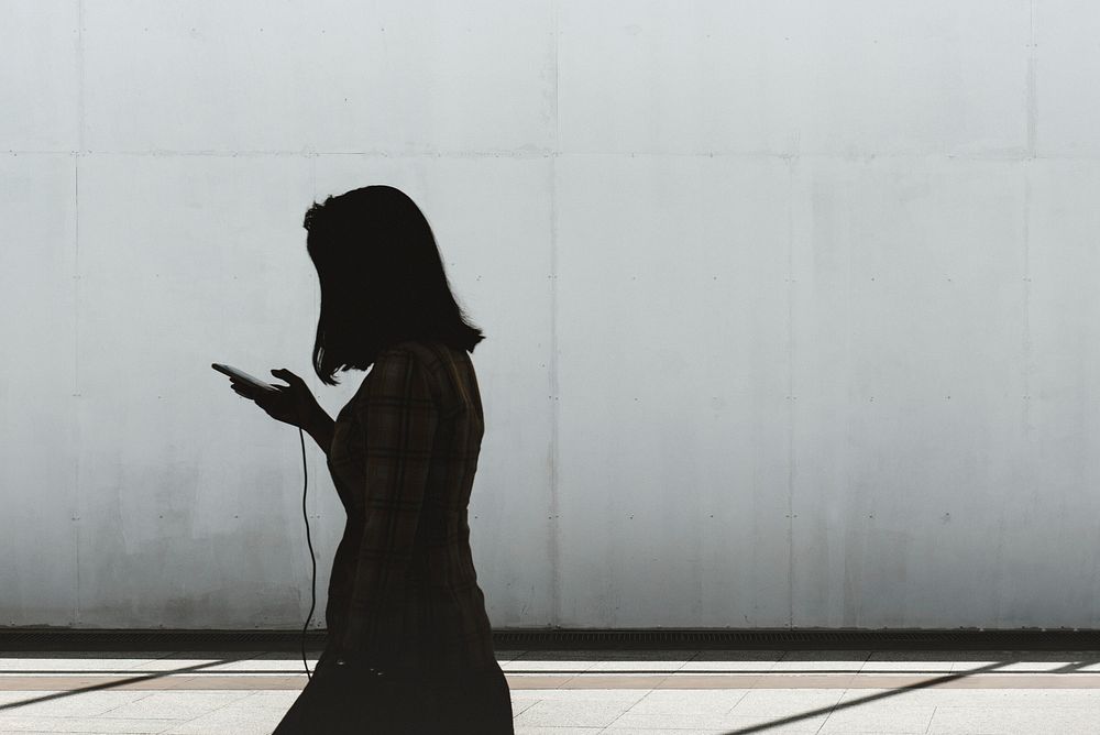 Silhouette of woman scrolling on her phone while walking