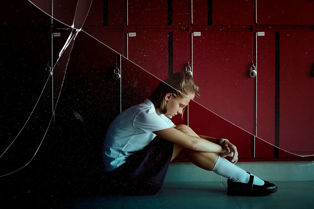 Depressed high school girl sitting by lockers in hallway with cracked glass effect
