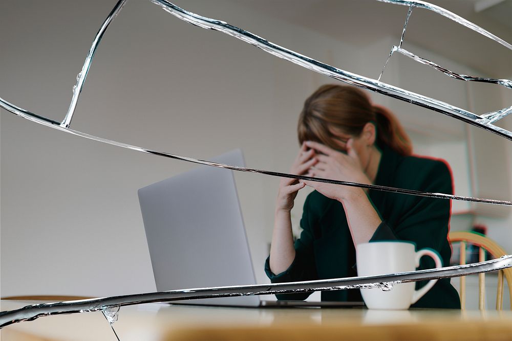 Stressed woman sitting in front of laptop with cracked glass effect