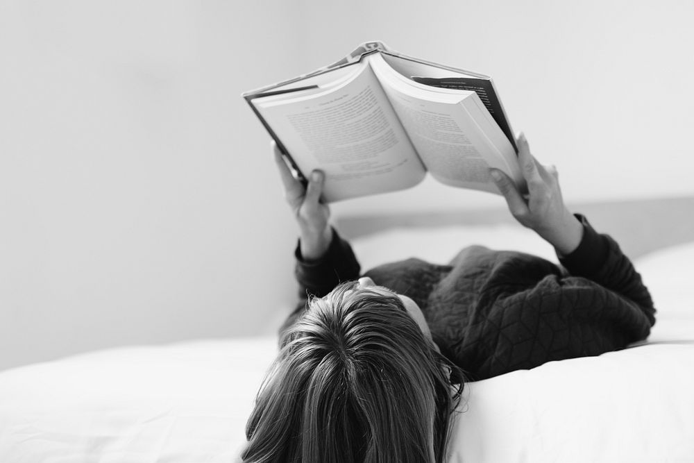 Woman reading a book on her bed in black and white