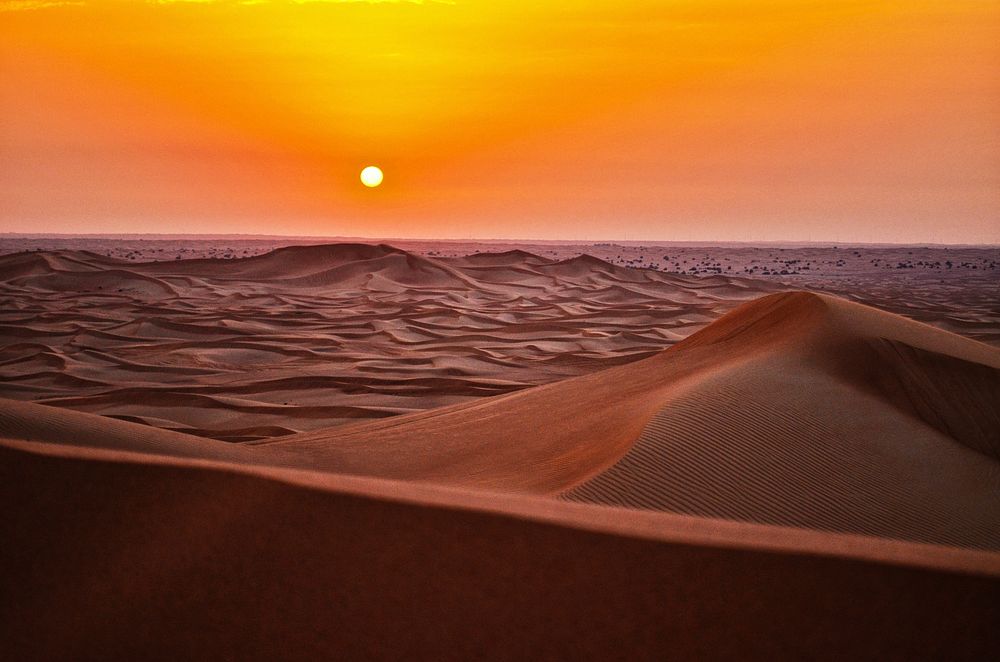 The sun setting over the sand dunes in the barren desert. Original public domain image from Wikimedia Commons