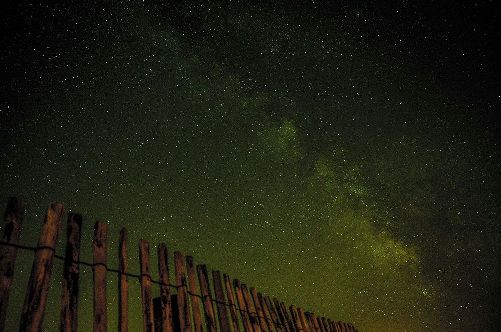 Bright stars in a green-hued sky over a wooden fence. Original public domain image from Wikimedia Commons