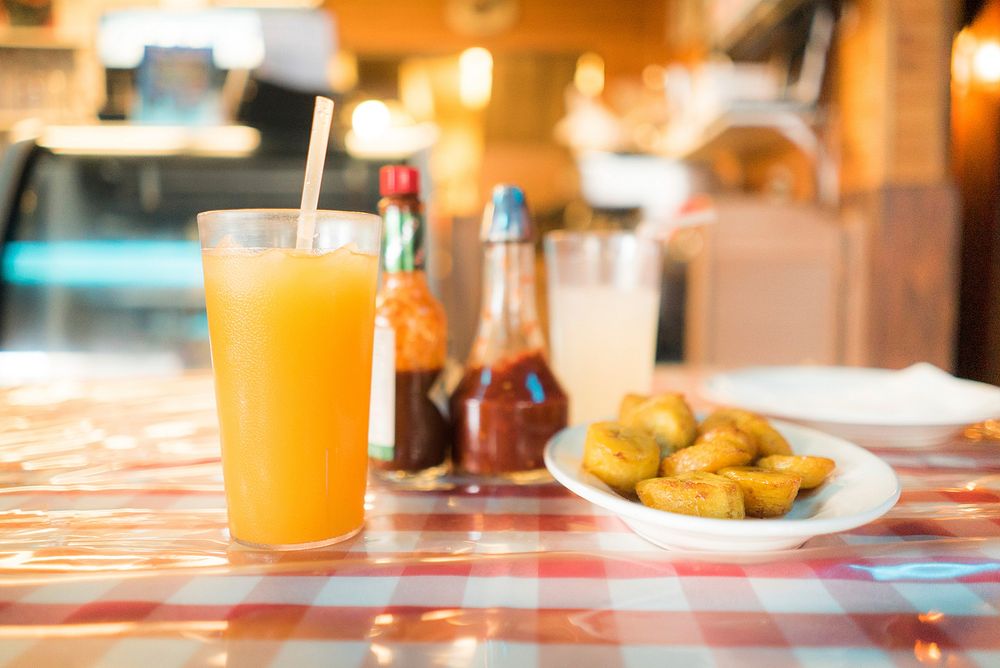 Fried potatoes next to a glass of juice and sauce bottles on a restaurant table. Original public domain image from Wikimedia…