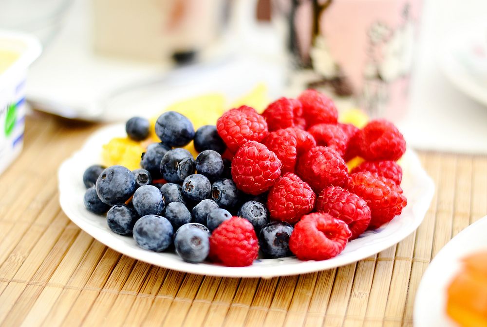 Plate of fresh fruit with raspberries and blueberries on a picnic table. Original public domain image from Wikimedia Commons