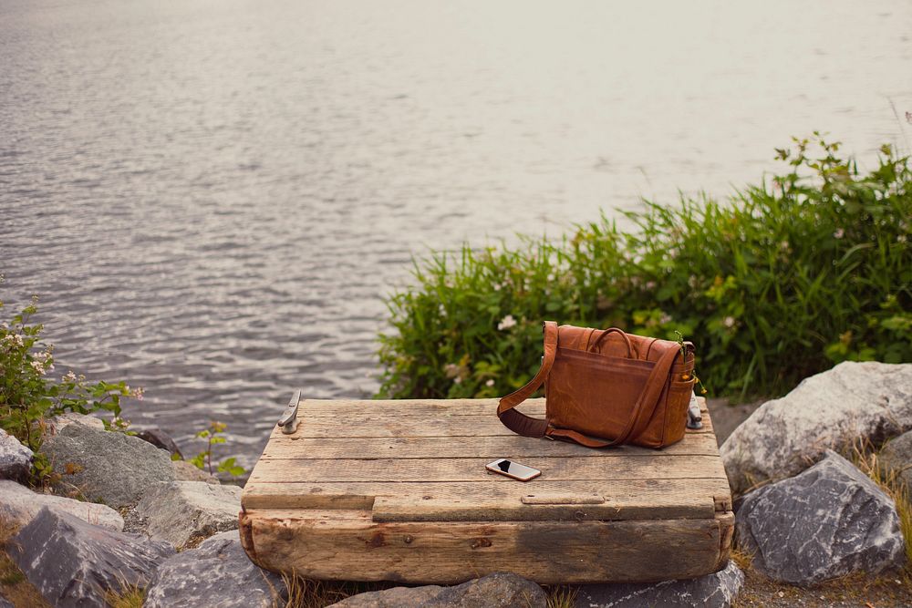 An iPhone cellphone and messenger bag on a wooden platform overlooking the water in Gas Works Parks. Original public domain…