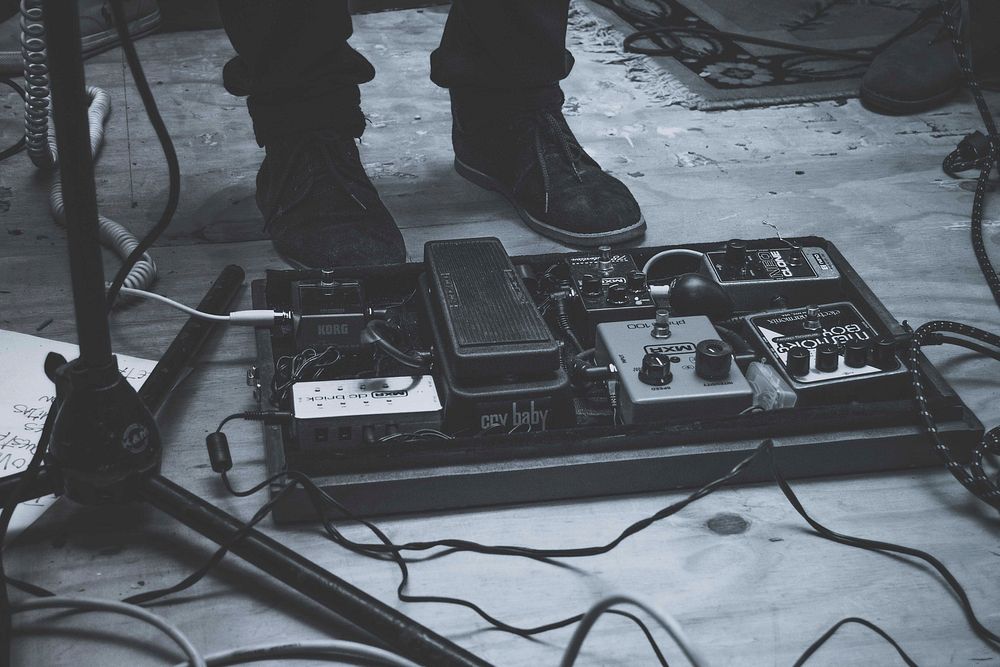 A low black-and-white shot of music equipment next to a person's shoes on stage. Original public domain image from Wikimedia…
