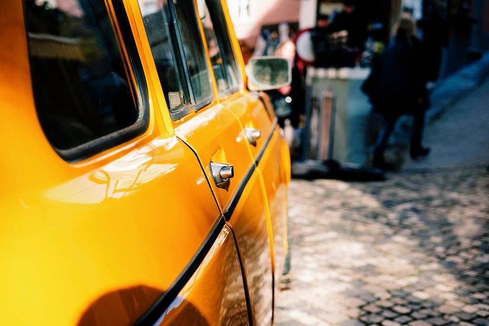 Side of a yellow car with people in the background. Original public domain image from Wikimedia Commons