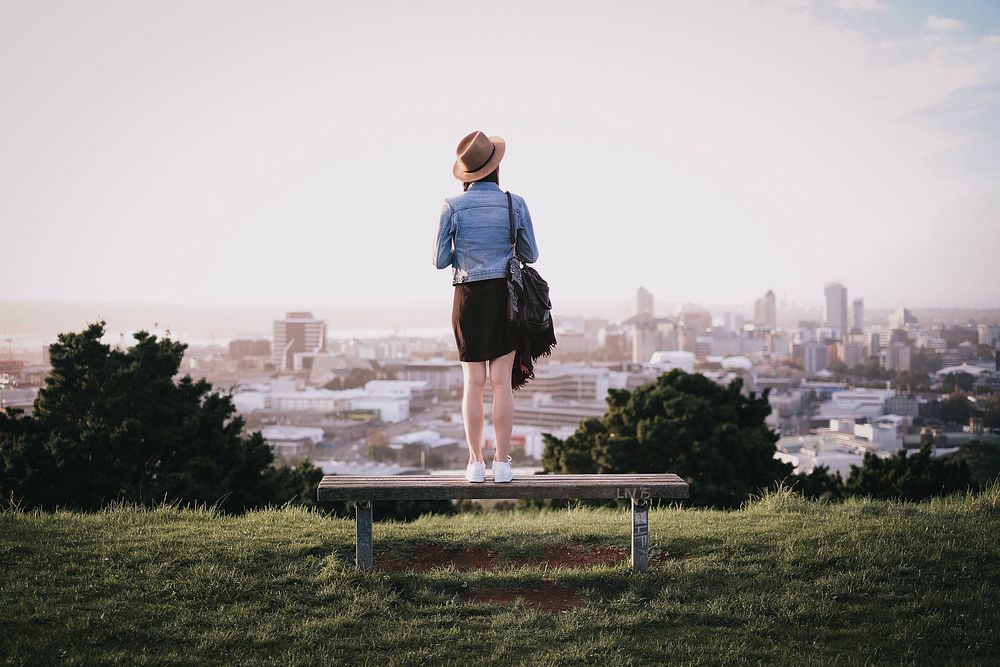 Woman standing on a park bench and surveying the city below. Original public domain image from Wikimedia Commons