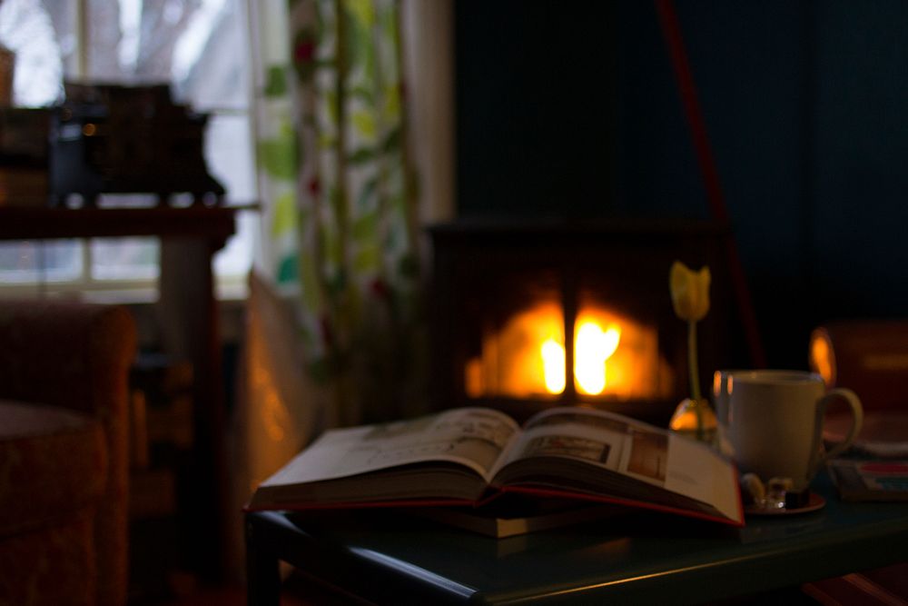 A book and coffee mug sitting on a table in a cozy den lit by firelight. Original public domain image from Wikimedia Commons
