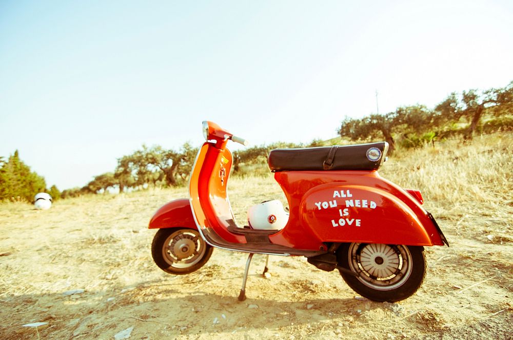 A motorscooter reading "ALL YOU NEED IS LOVE" sits a dry grassy area in Caltagirone. Original public domain image from…
