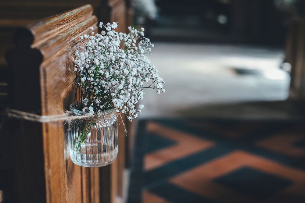 White baby's-breath flowers in a glass jar attached to a church pew. Original public domain image from Wikimedia Commons
