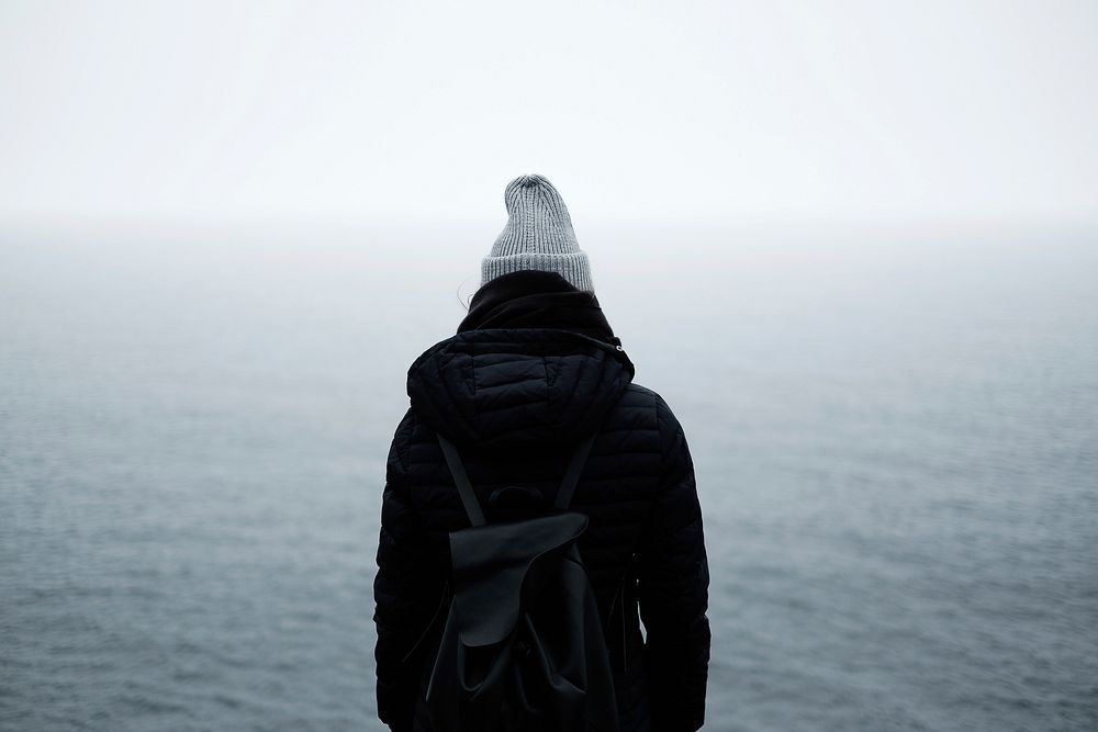Person in winter wear with backpack watches misty water in Cape Spear. Original public domain image from Wikimedia Commons