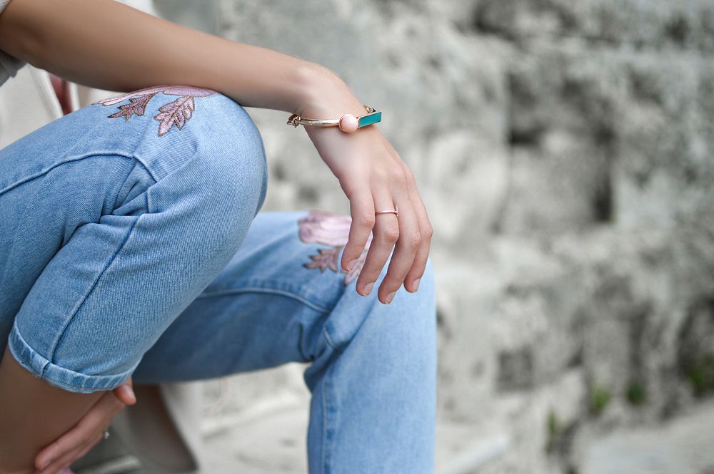 A seated woman in jeans with a bracelet on her wrist. Original public domain image from Wikimedia Commons